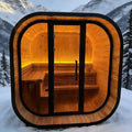 Elevate Performance Systems Noir Cube Sauna with black exterior, glass front, and warm LED-lit spruce interior in snow.