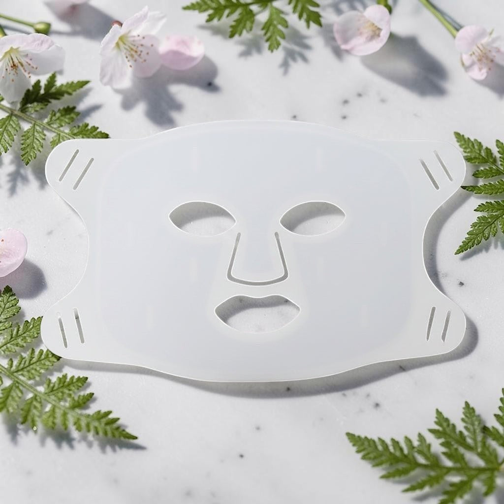 Elevate Performance Systems white silicone light therapy facial mask on a marble surface with flowers and ferns.