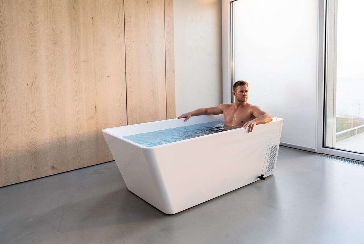 Man relaxing in an Elevate Performance Systems white cold plunge tub on a luxury patio with mountain views at sunset.